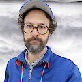 Portrait of Andrés Galeano. He is wearing glasses, a cap and a blue jacket.