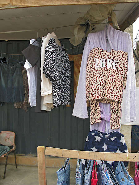 Verschiedene Kleidungsstücke hängen an Kleiderbügeln an einem Marktstand. Sie hängen auf Kopfhöhe. Rechts im Bild  hängt ein Oberteil in Leopardenmuster mit der Aufschrift LOVE.